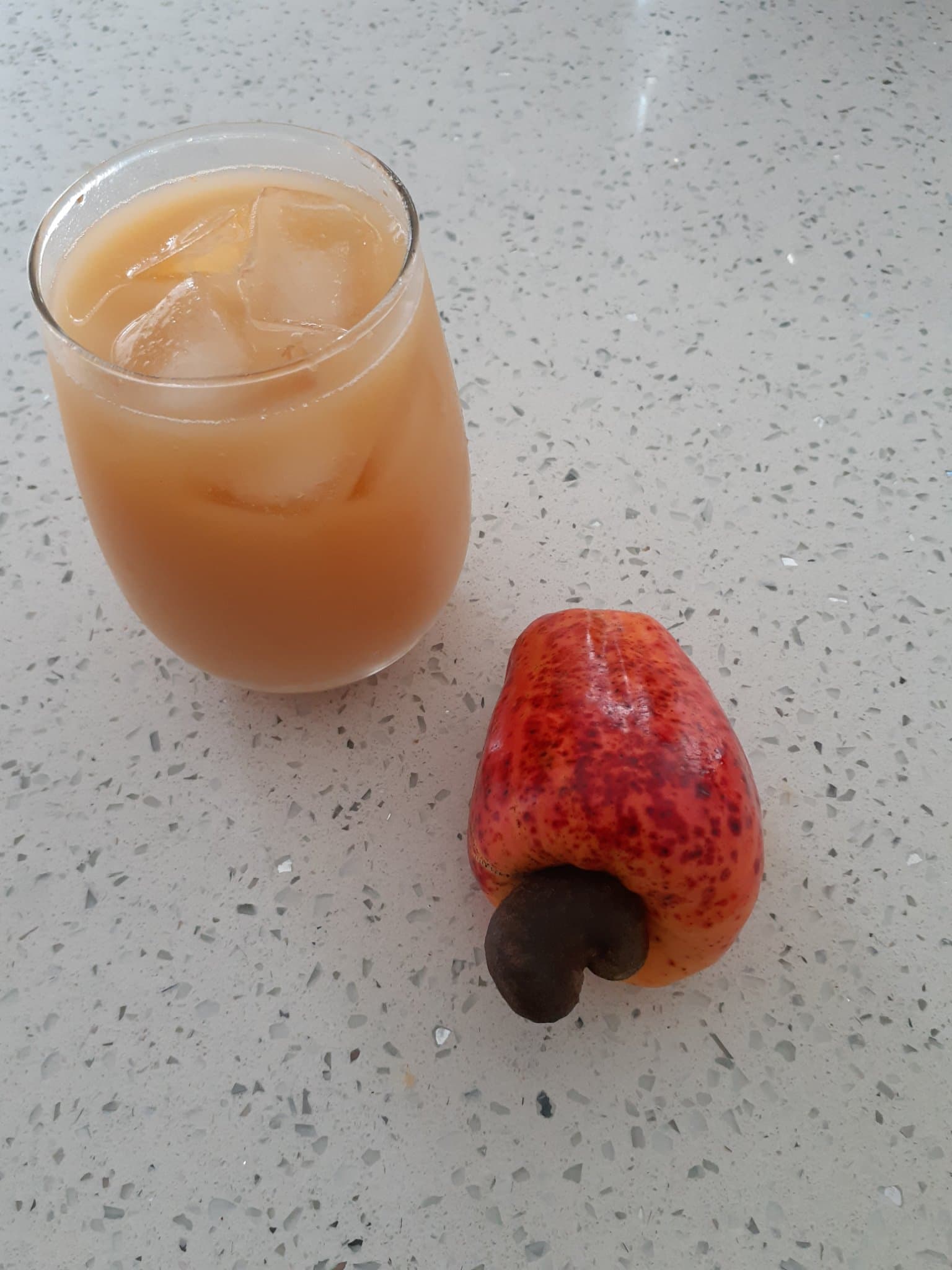 A fresh cashew apple next to a glass of homemade cashew juice over ice, the finished result